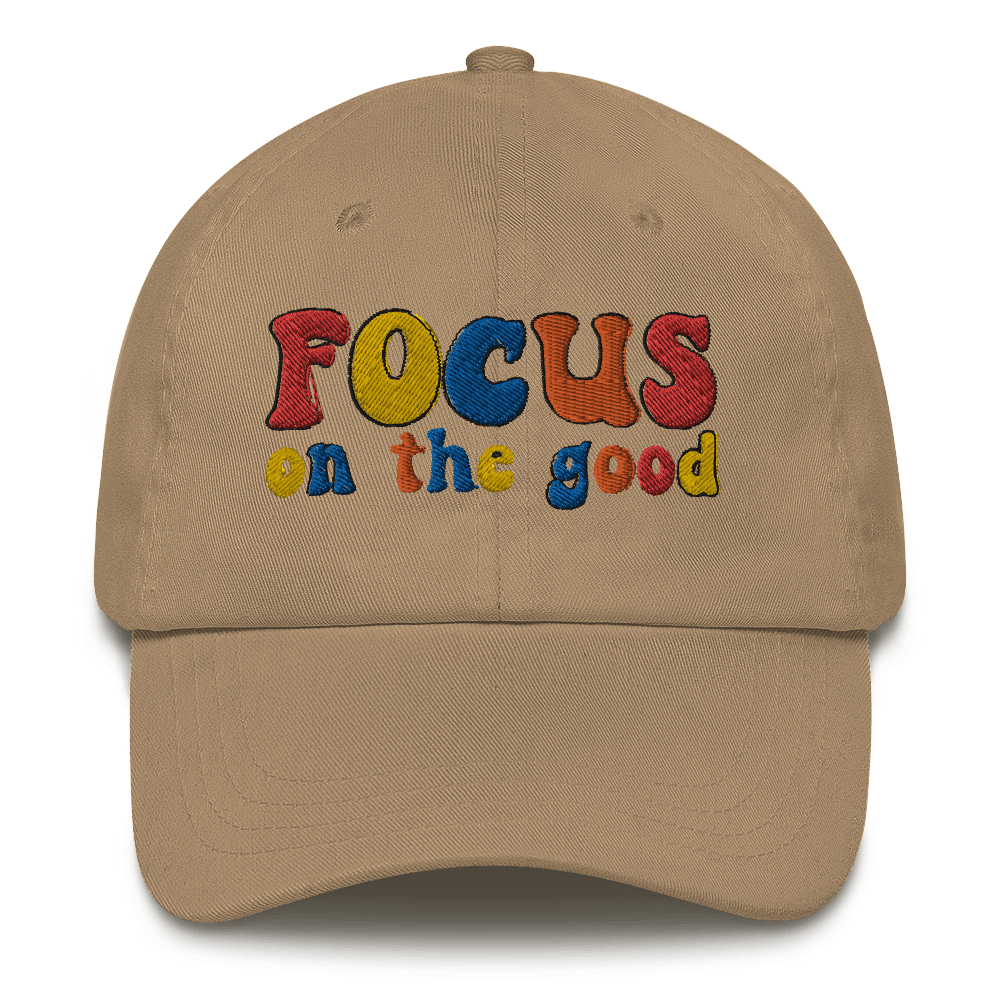 A beige baseball cap with 'FOCUS on the good' text embroidered in multiple colors on the front.