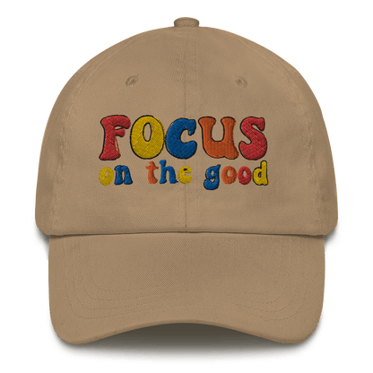 A beige baseball cap with 'FOCUS on the good' text embroidered in multiple colors on the front.
