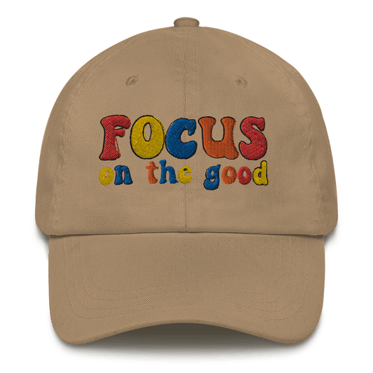A beige baseball cap with 'FOCUS on the good' text embroidered in multiple colors on the front.