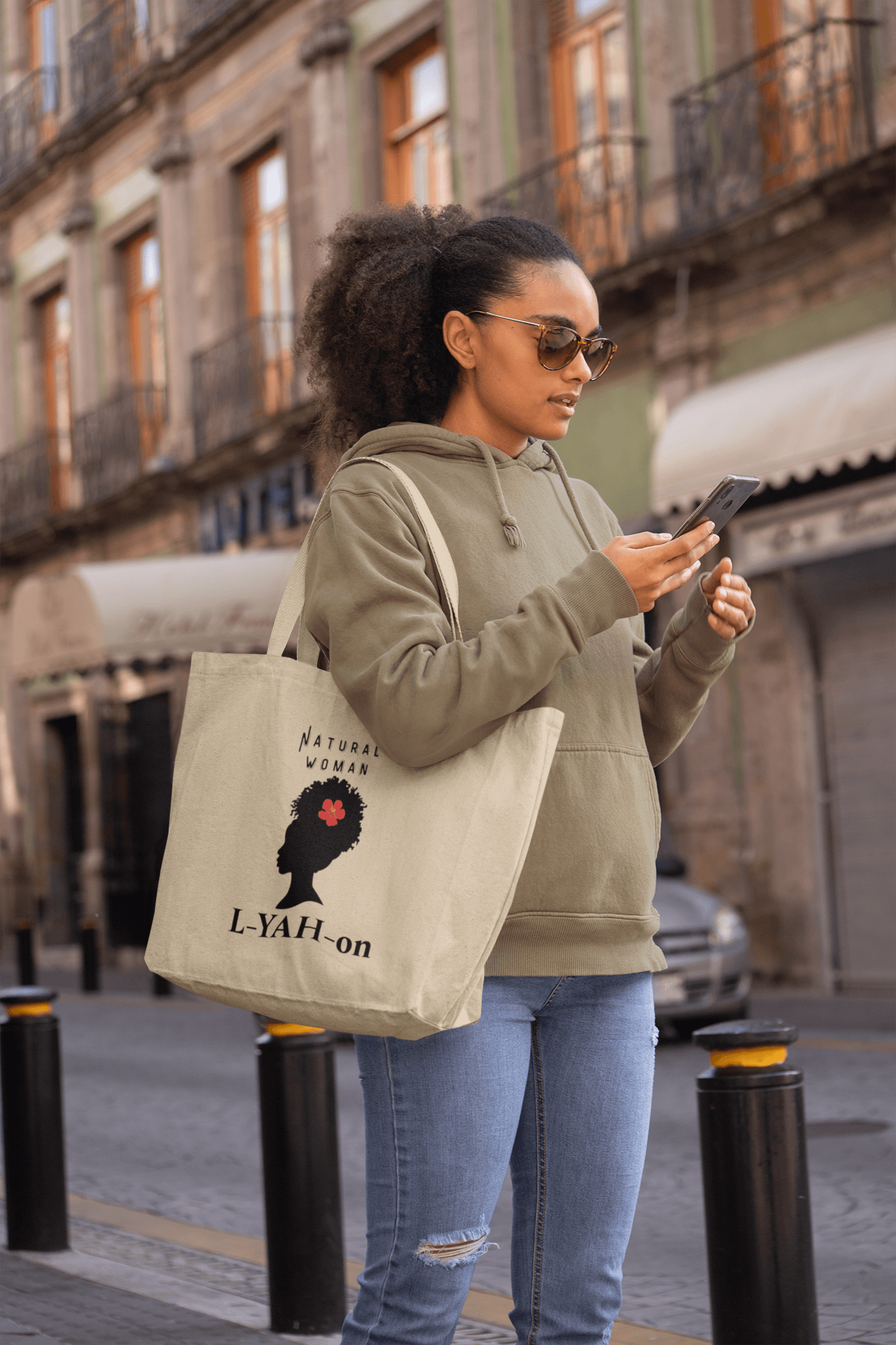 Woman holding a tote bag with a design and text, standing on a street.