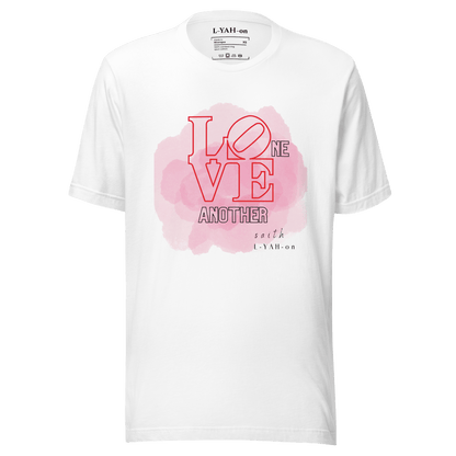 A pink crew neck t-shirt with the text 'LOVE ONE ANOTHER' printed in the center.